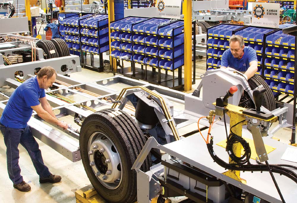 Two assembly line employees work on a vehicle chassis. 