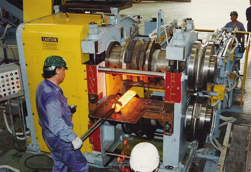 Employee feeds a hot metal roll into processing machine.