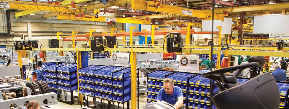 Assembly line with employees and multiple blue bins of various parts and components.