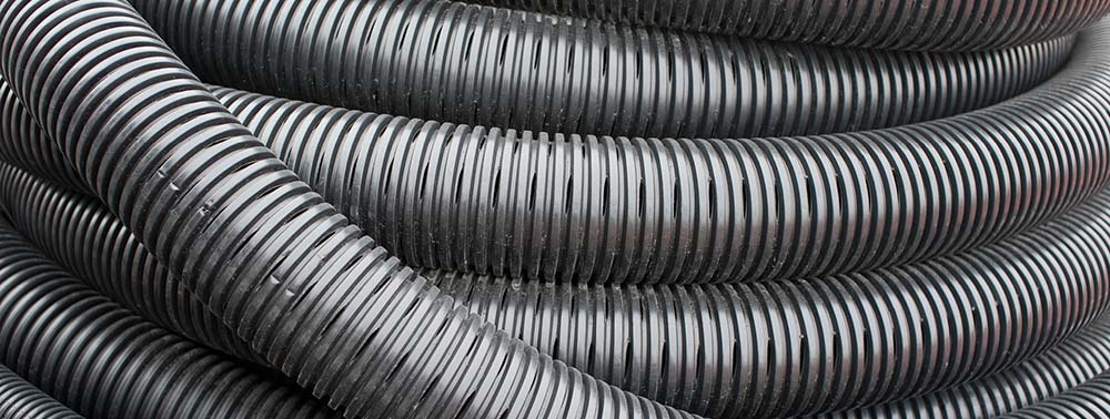A black, ridged pattern hose assembly is coiled into a circle, stacking on itself.