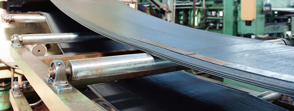 Sheets of silver metal lying across industrial rollers on a conveyor belt
