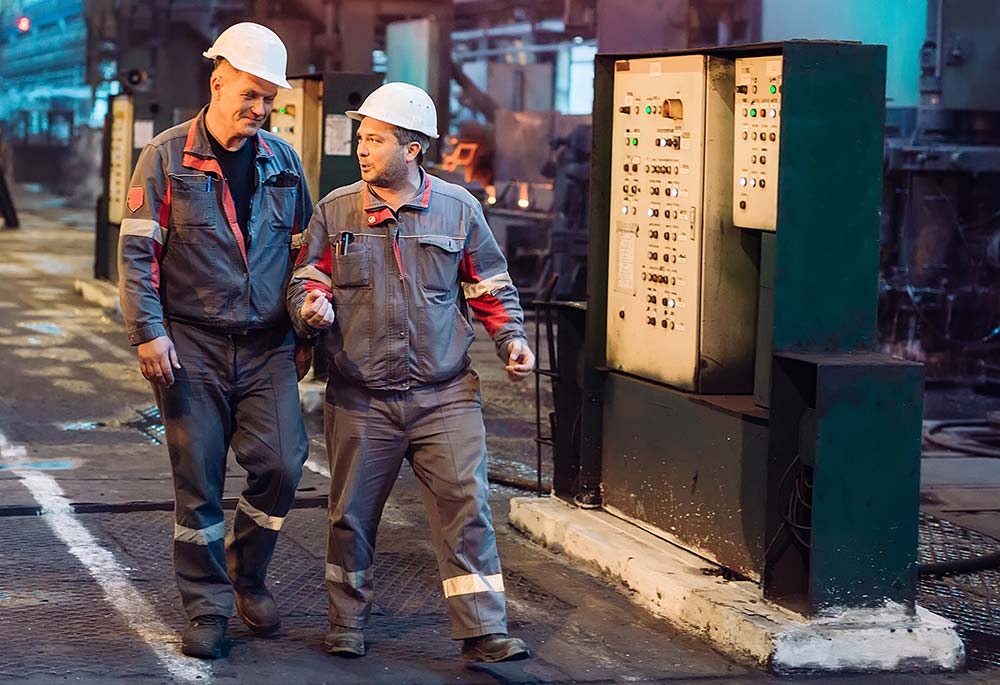 Two workers in hardhats walk across a factory floor