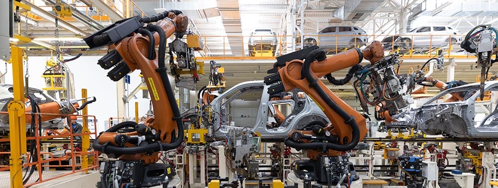 Robotic arms welding vehicle bodies on automotive assembly line.